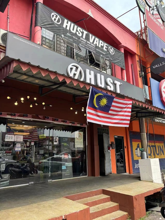 Photo of the Hust Vape shop in Malaysia, featuring the storefront with a Malaysian flag, showcasing the local vape retail scene.